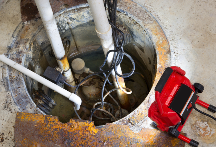 A sump pump in a basement with a red LED light illuminating the pit and pipe work for draining ground water